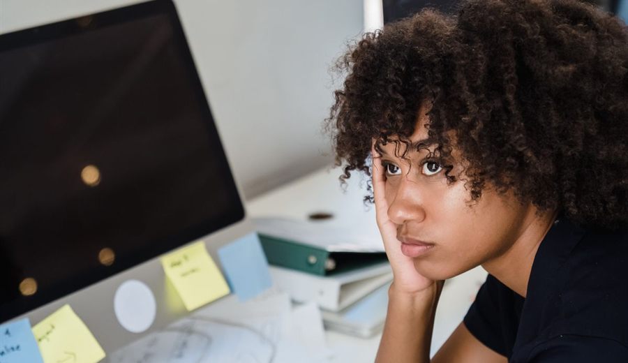 Mujer distraída frente a su escritorio con notas adhesivas y computador